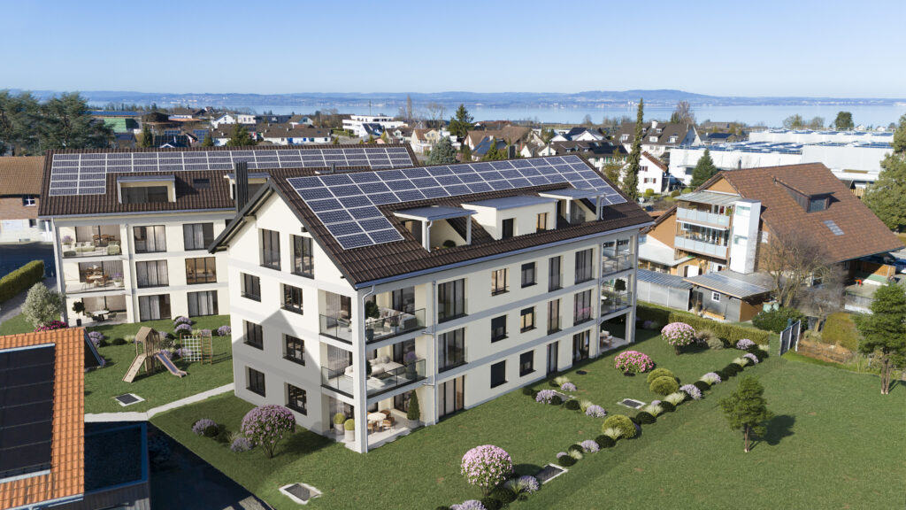Apartment complex with extensive rooftop solar panels and a landscaped lawn, overlooking a lakeside town.